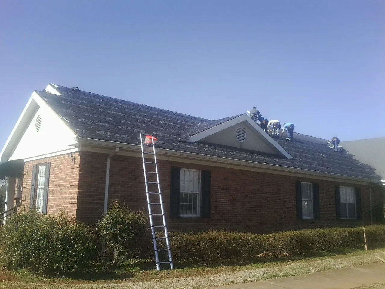 Crew tearing shingles off a brick ranch roof with a ladder set — Metal Roof Repair work by our crew in Terre Haute
