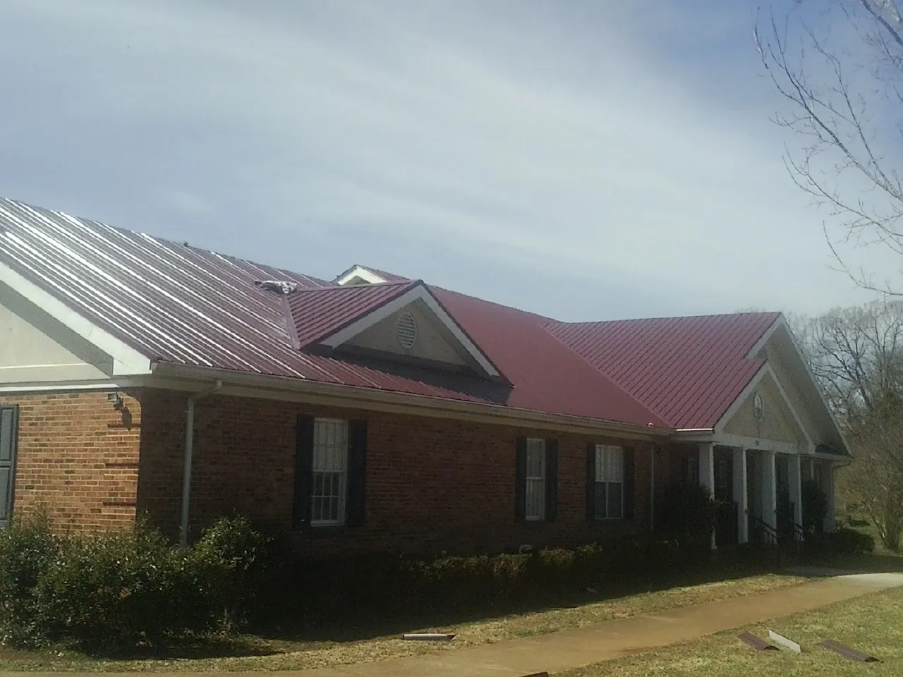 Red metal roof with gabled entries on a long brick building, from a Hail Damage Roof Repair job in Terre Haute