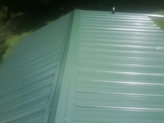 New green metal panels meeting at the ridge of a roof — Flat Roof Repair work by our crew in Terre Haute