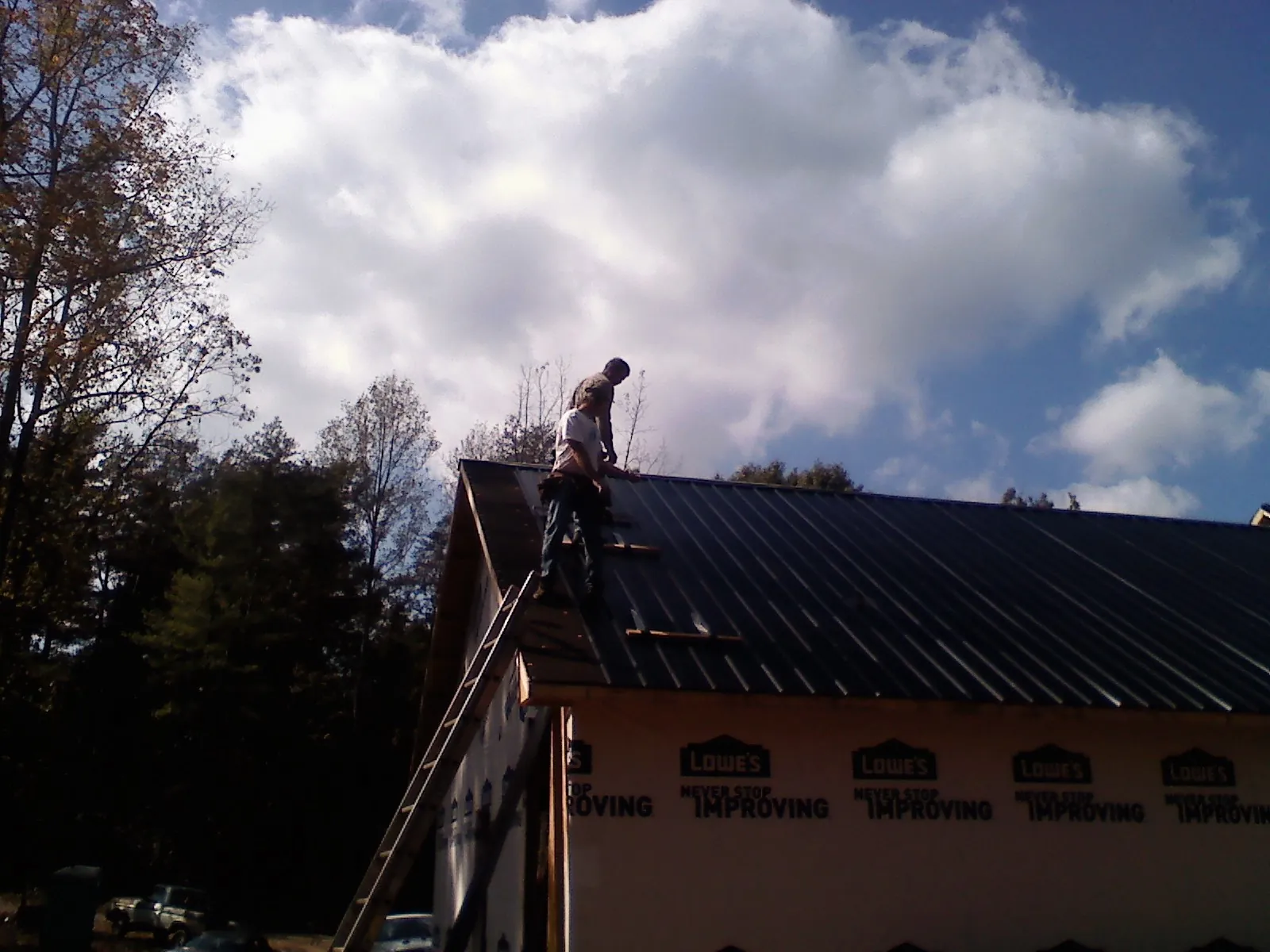 Roofer fastening dark metal panels high against a cloudy sky, from a Roof Inspection job in Terre Haute