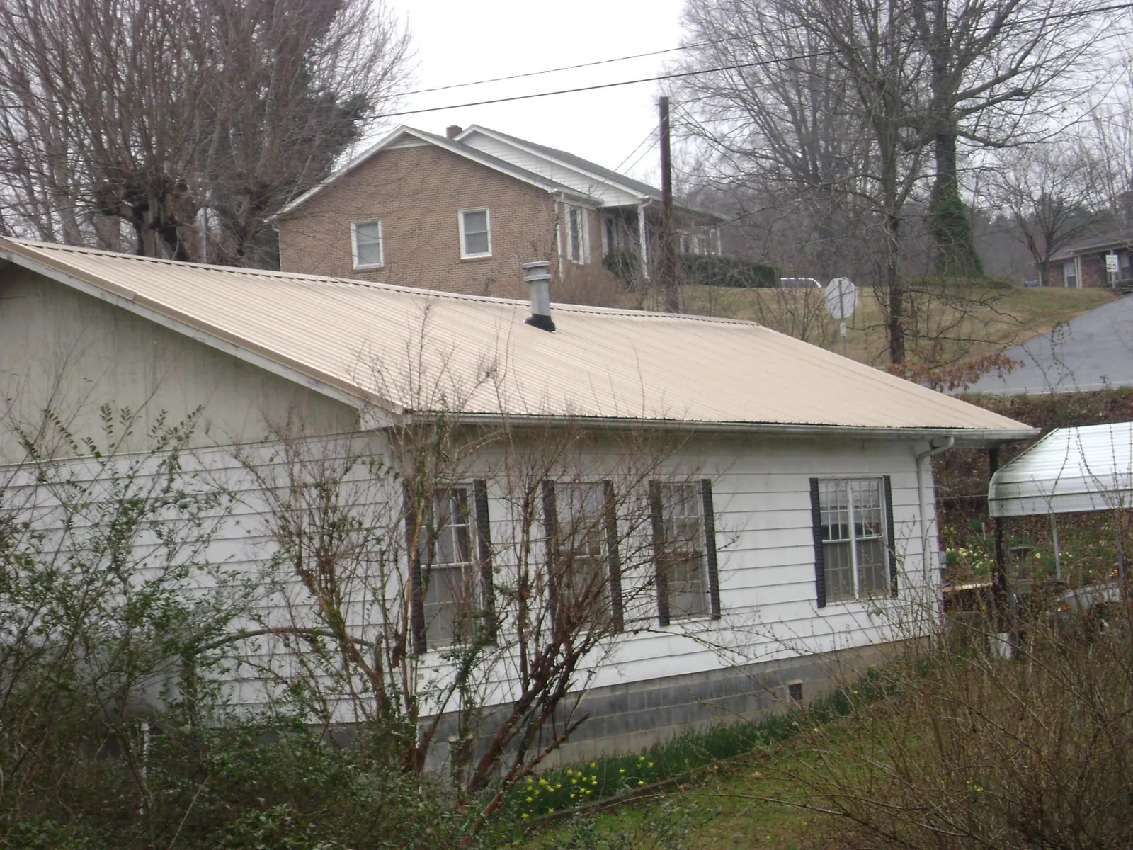 Tan metal roof on a white sided house set into a hillside — Commercial Roofing by Roofing Brothers in Terre Haute