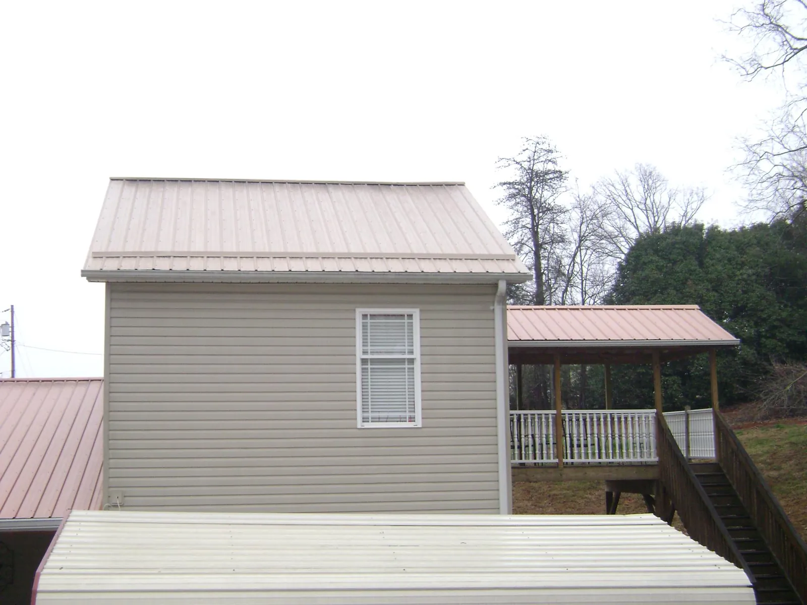 Tan metal roofs on a two story addition and attached porch, from a Roof Replacement job in Terre Haute